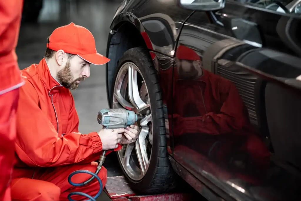Technician using an impact wrench on a black car's alloy wheel