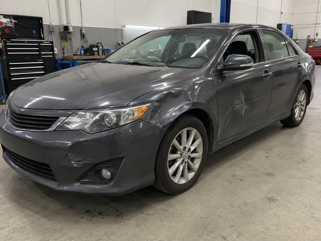 Dark grey sedan with dents in the front wing, door and bumper before repair