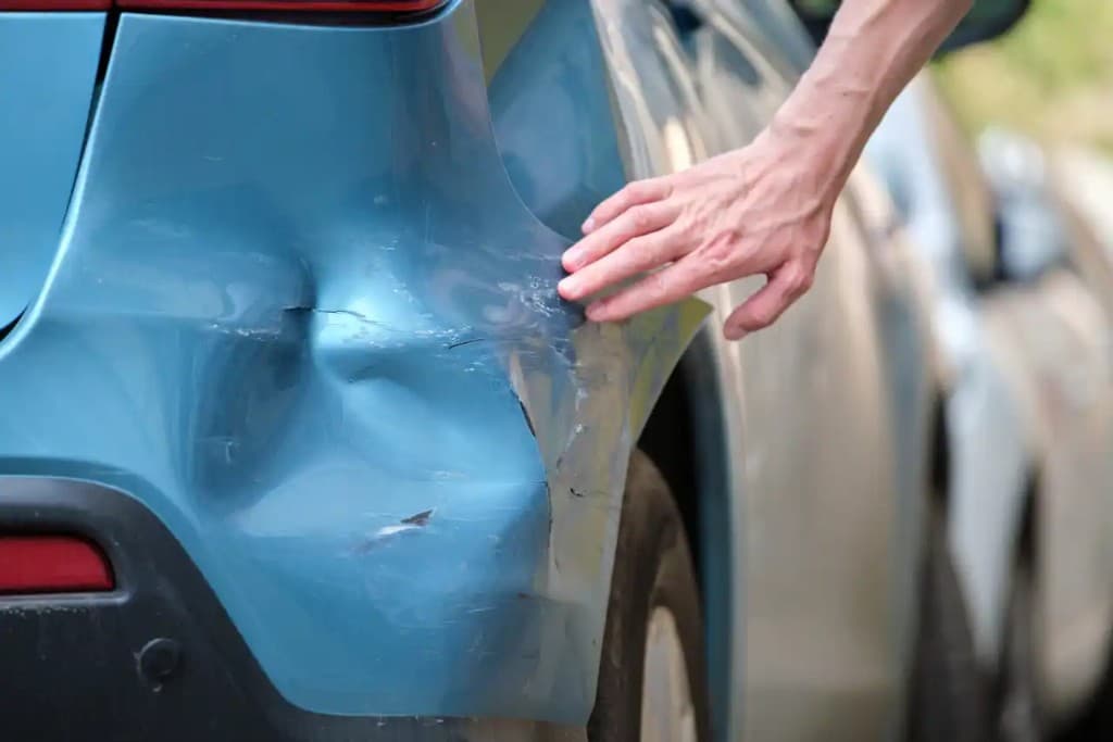 Hand inspecting a large dent and scratches on a blue car panel