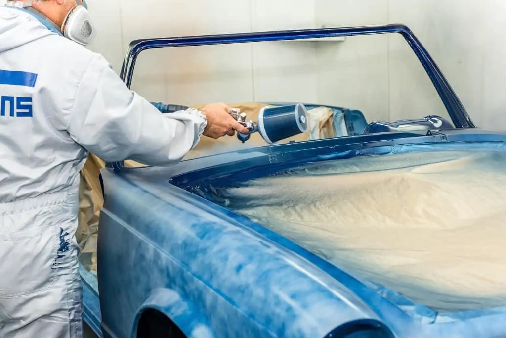 Technician in a spray booth painting a classic blue car during restoration