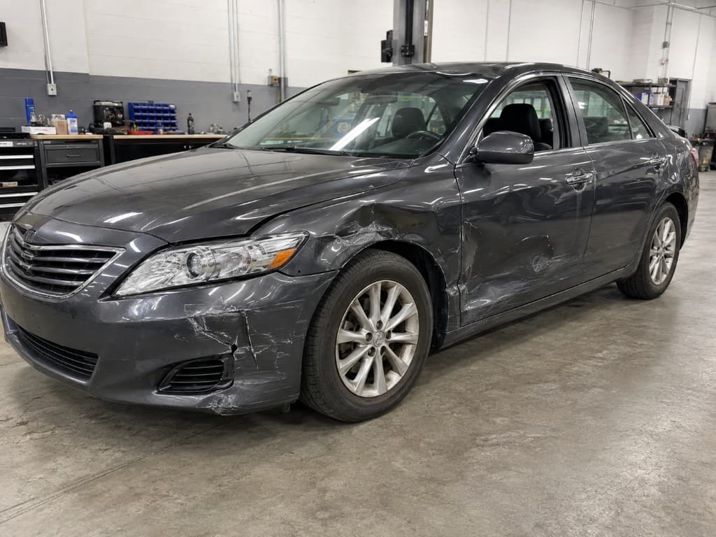 Dark grey sedan with crumpled wing, door dent and bumper damage before body repair