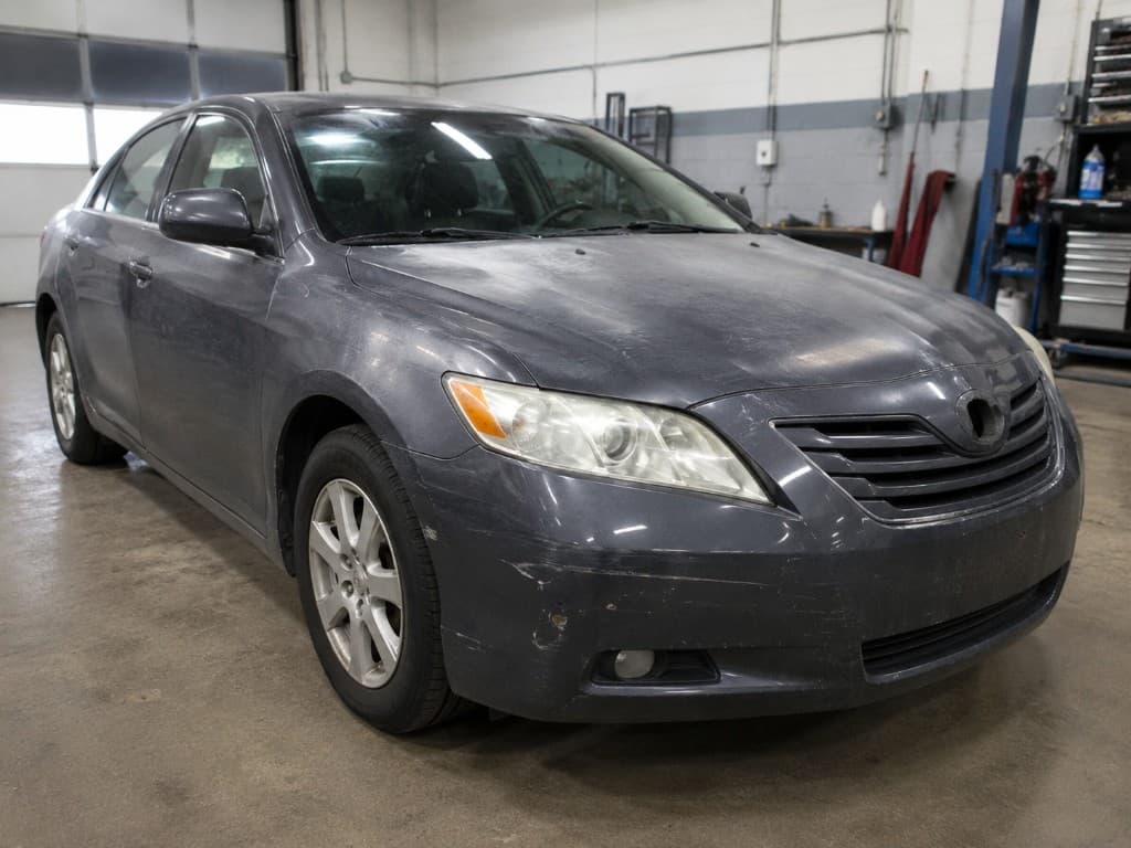 Dark grey sedan with dull, oxidised paint and bumper scuffs before refinishing